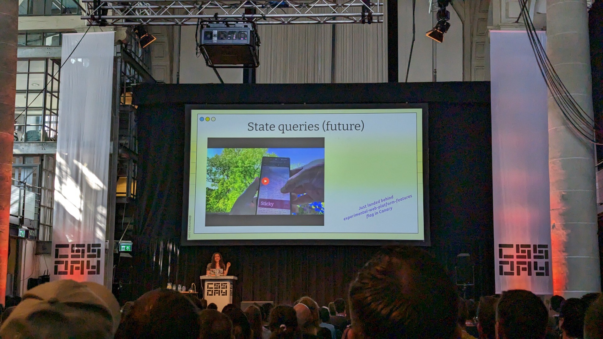 Una Kravets on stage at CSS Day, with a slide that shows The stuck state query in Chrome Canary
