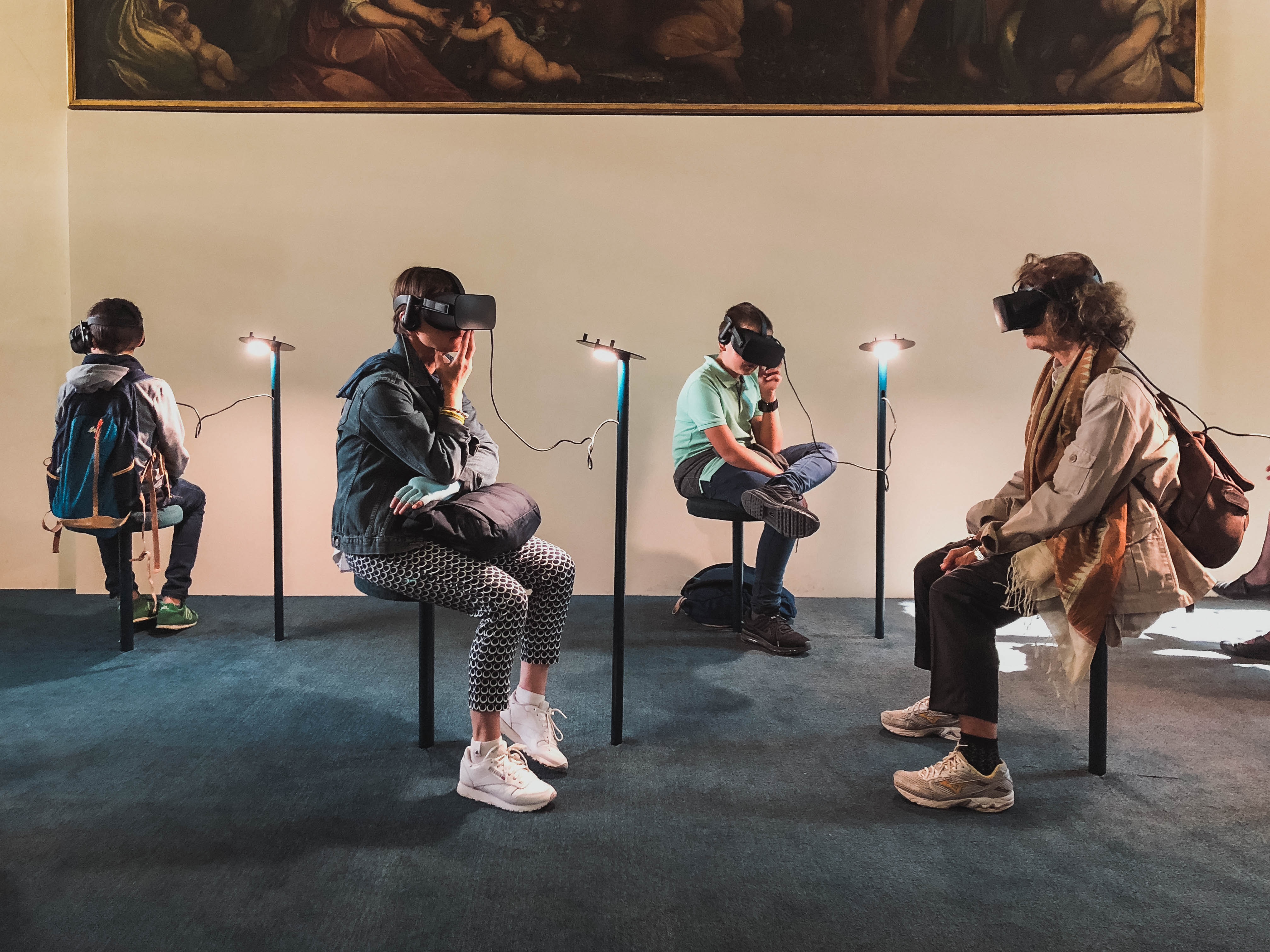 four people sitting in a room
wearing virtual reality headsets
wired to posts next to them,
and all facing different directions
