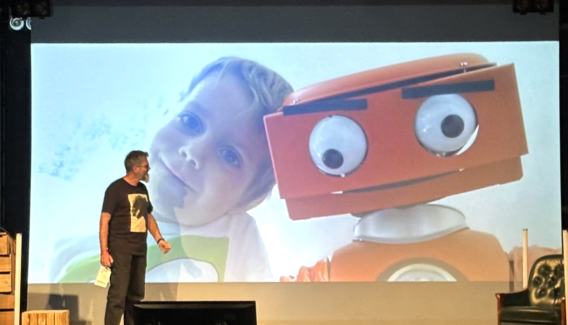 Jan in front of a slide of his young child and an orange-faced robot leaning their heads together
