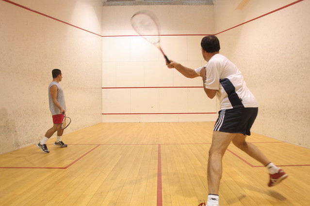 Two guys in a squash court, the closer one is taking a dramatic swing
